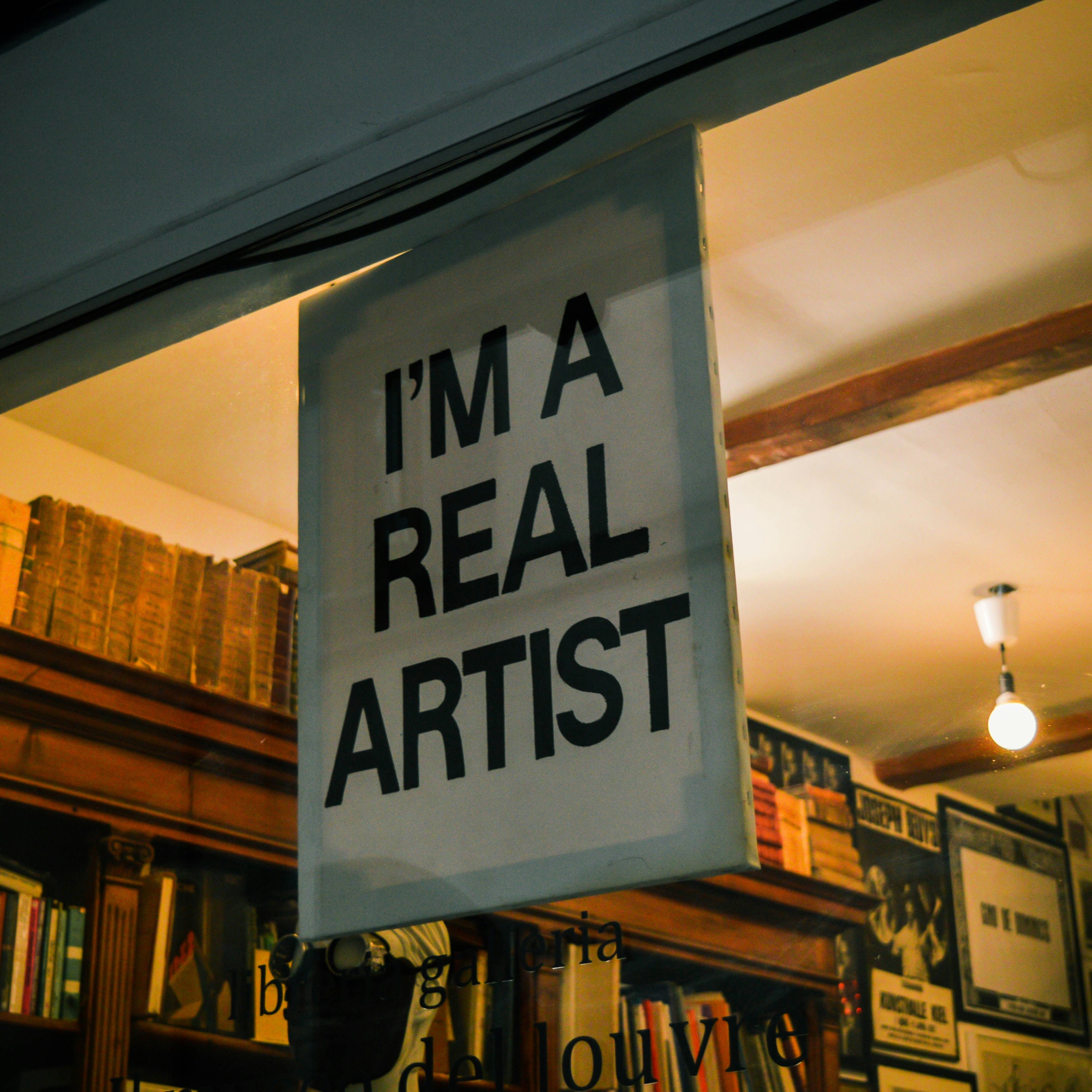 Sign inside a room with books and artwork, stating 'I'm a real artist'.